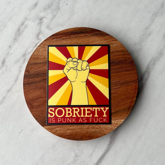 Wooden coaster with a Sticker with a fist and text 'Sobriety is punk as fuck' on a marble surface