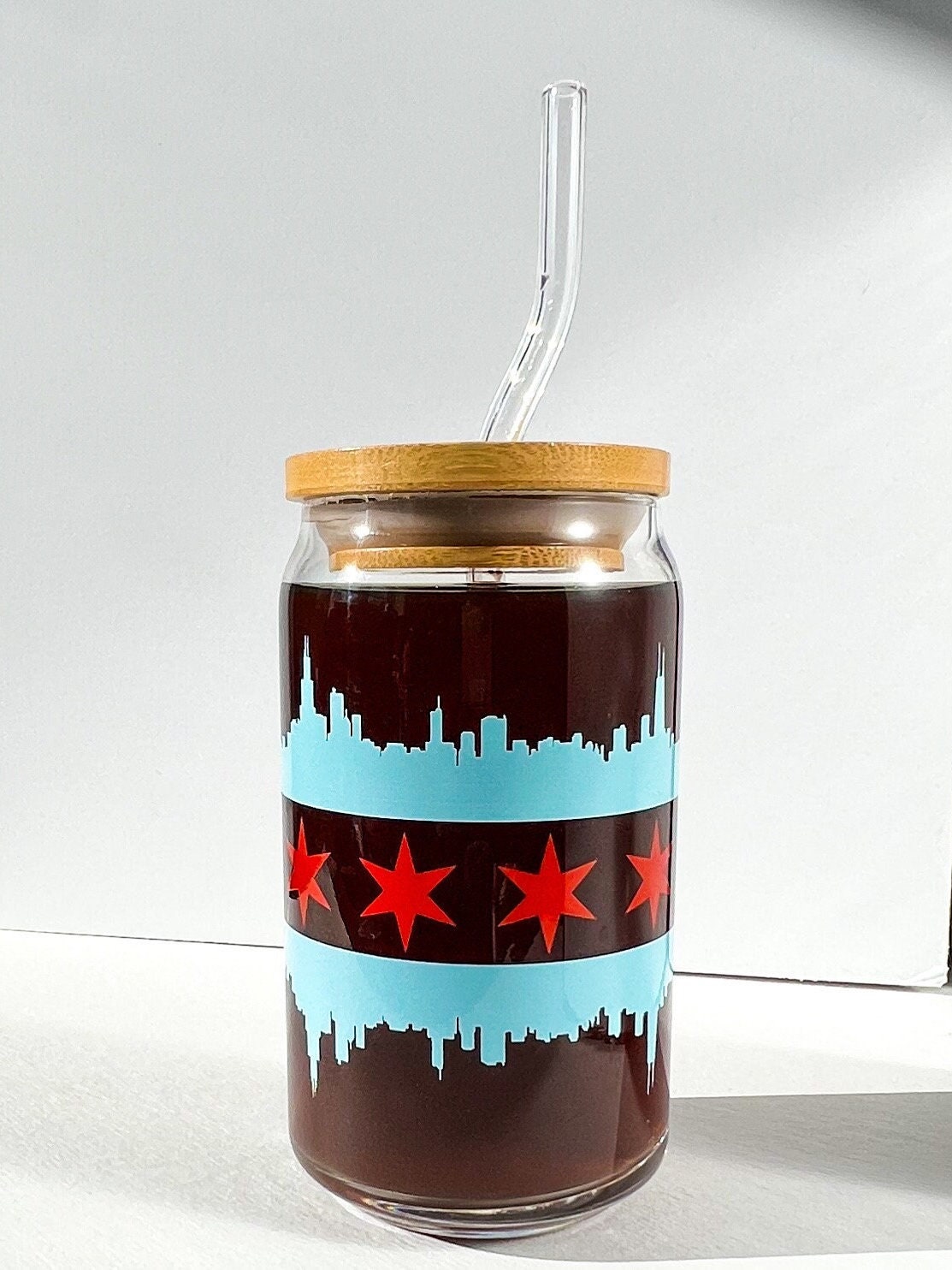 Glass tumbler with wooden lid and straw, featuring a design of stars and a skyline in the design of the Chicago flag.