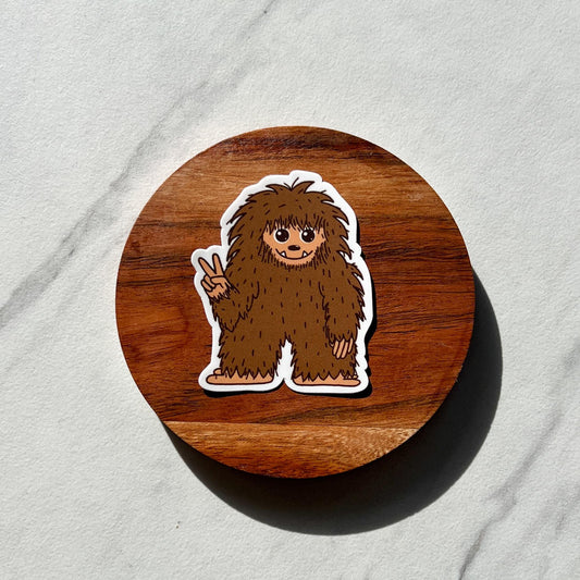 Wooden coaster Sticker of a fluffy Bigfoot making a peace sign on a light gray background