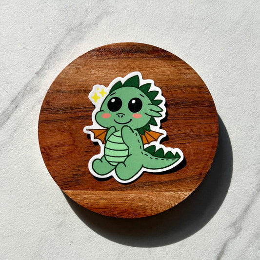 Cute green dragon sticker on a wooden round board with a light gray background