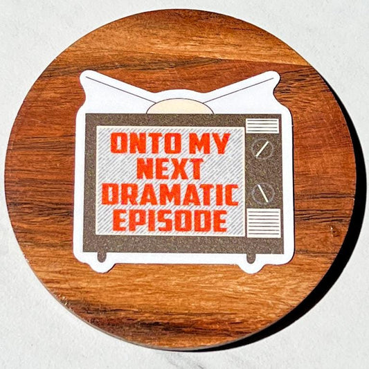Wooden coaster with a sticker with a retro TV sticker and text 'Onto my next dramatic episode'' on a white background