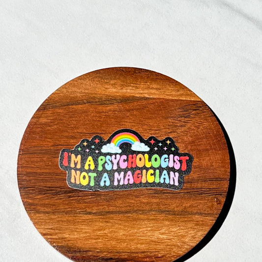 Wooden coaster with a colorful sticker reading 'I'm a psychologist not a magician' on a white background