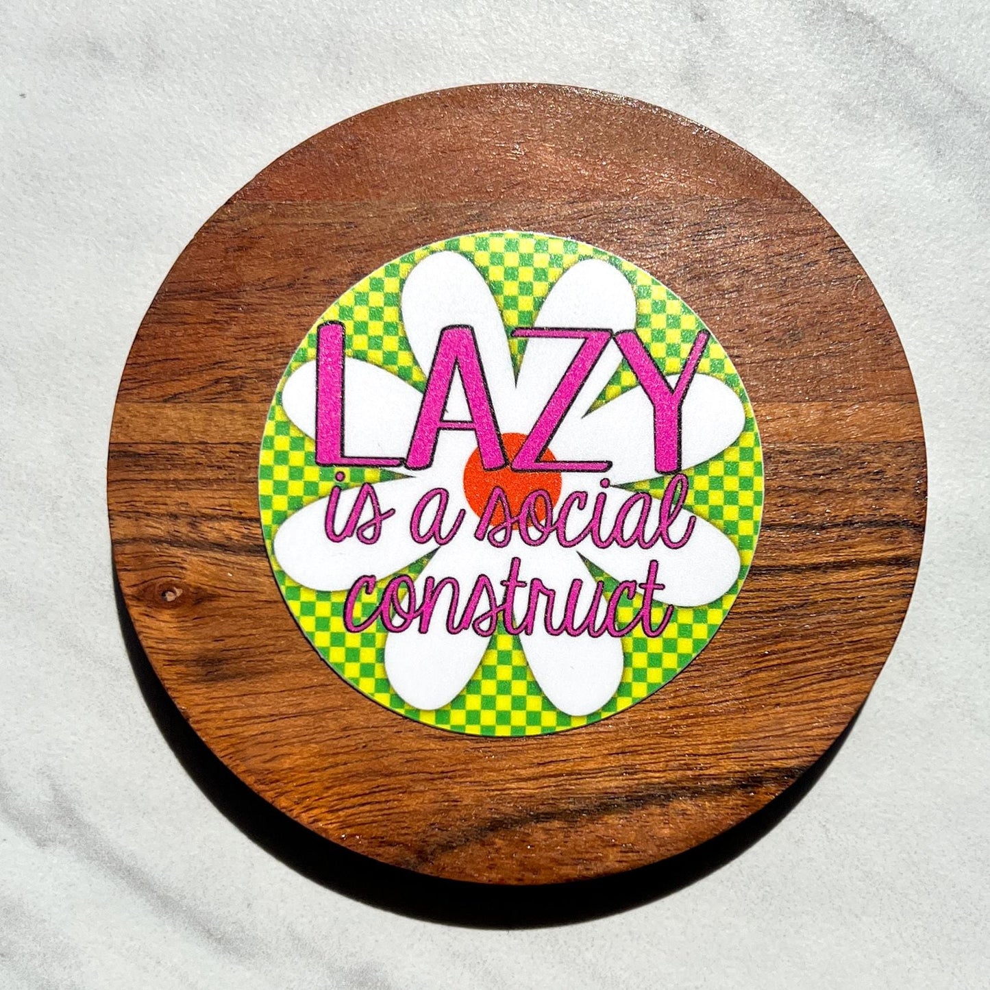 Circular sticker with 'Lazy is a social construct' text on a wooden background