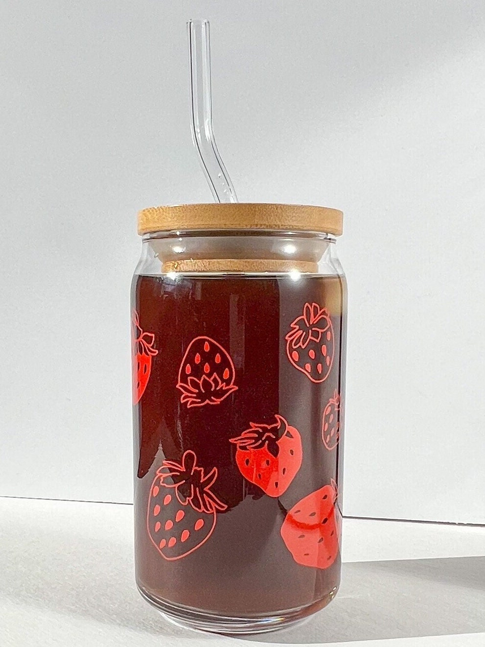 Glass jar with straw lid and strawberry pattern on a white background