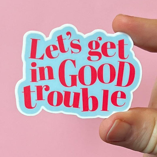 Sticker with 'Let's get in Good trouble' text held by a hand against a pink background