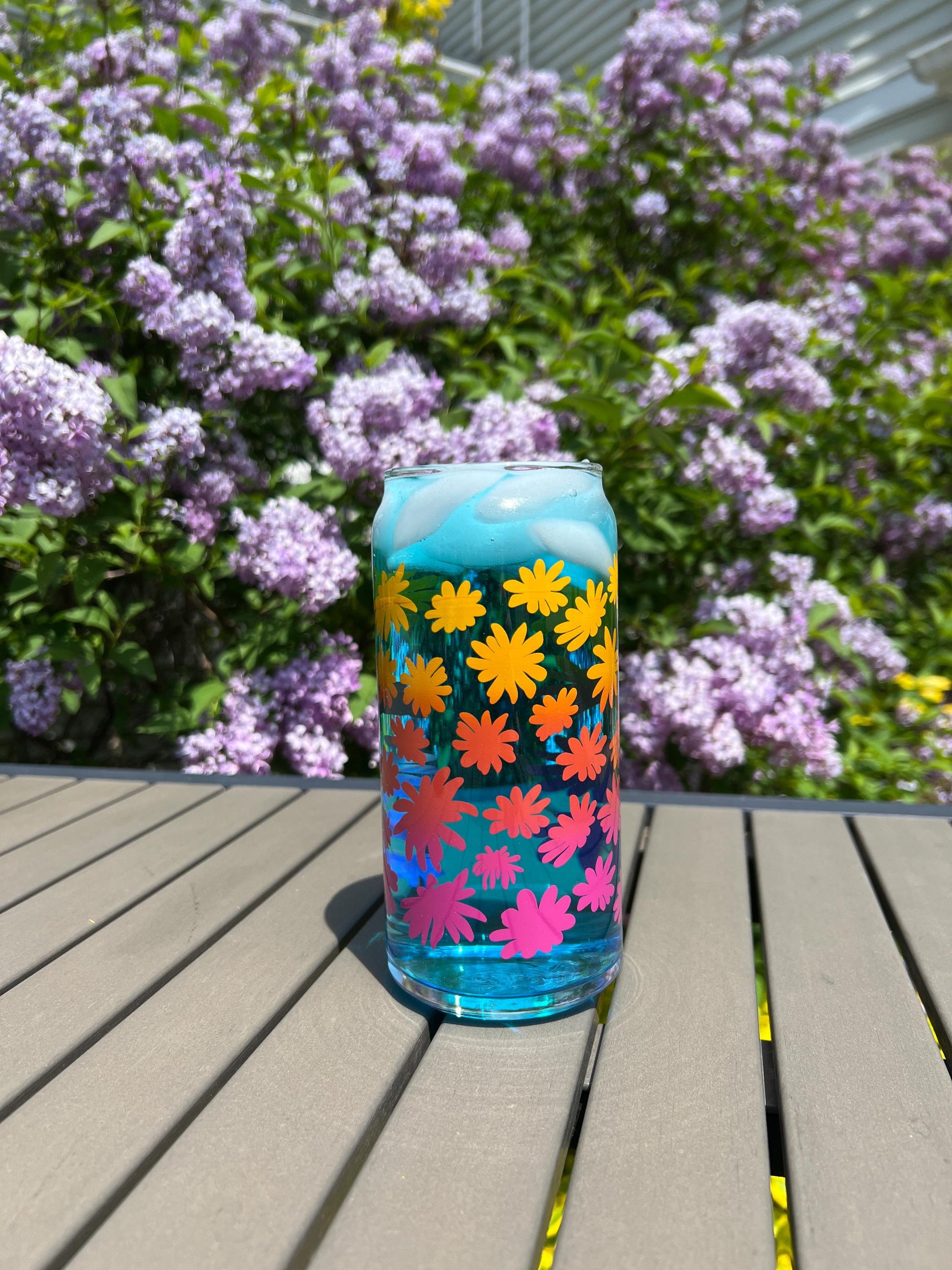 Colorful floral-patterned can on a wooden surface with purple flowers in the background