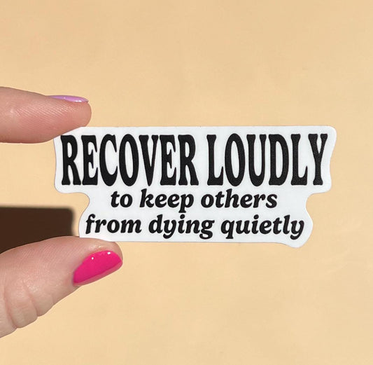 Sticker with text 'RECOVER LOUDLY to keep others from dying quietly' held by a hand on a beige background