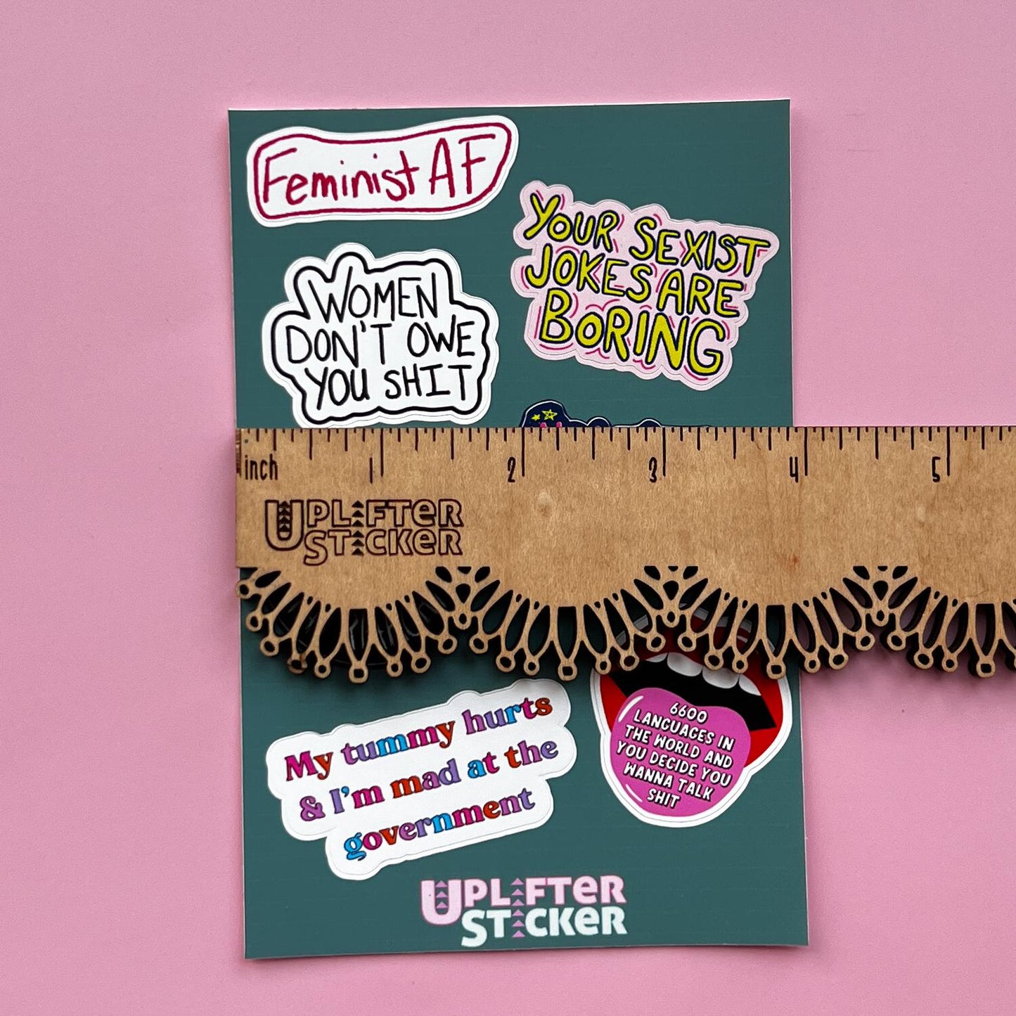 Sticker pack with various statements on a pink background, next to a ruler for size reference.
