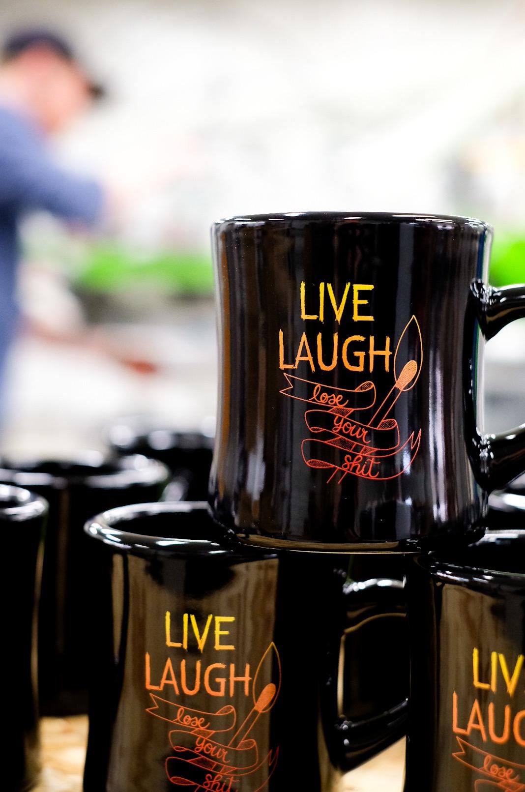 Black mug with 'Live Laugh Love Your Wife' text in orange on a reflective surface.