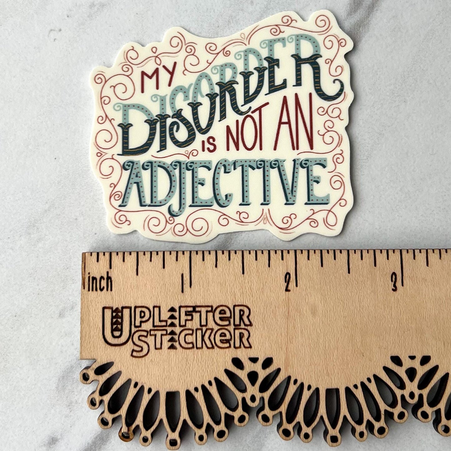 Sticker with decorative text 'My Disorder is Not an Adjective' next to a ruler for size reference.