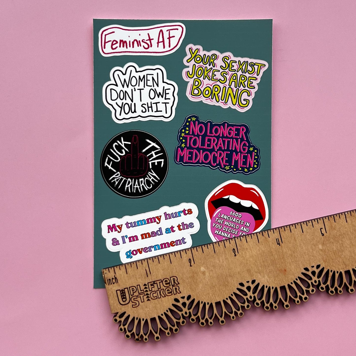 Sticker pack with various statements on a pink background, next to a ruler for size reference.