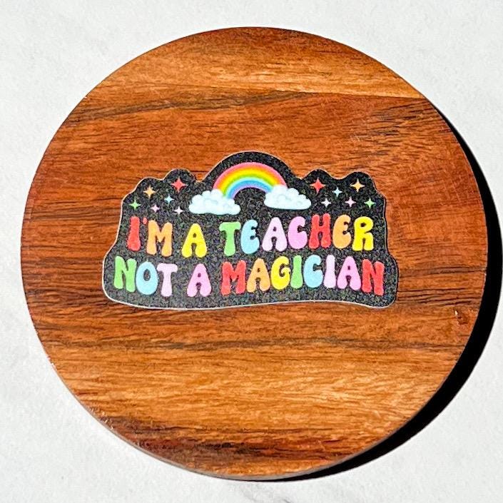 Wooden coaster with a colorful sticker reading 'I'm a teacher not a magician' on a white background