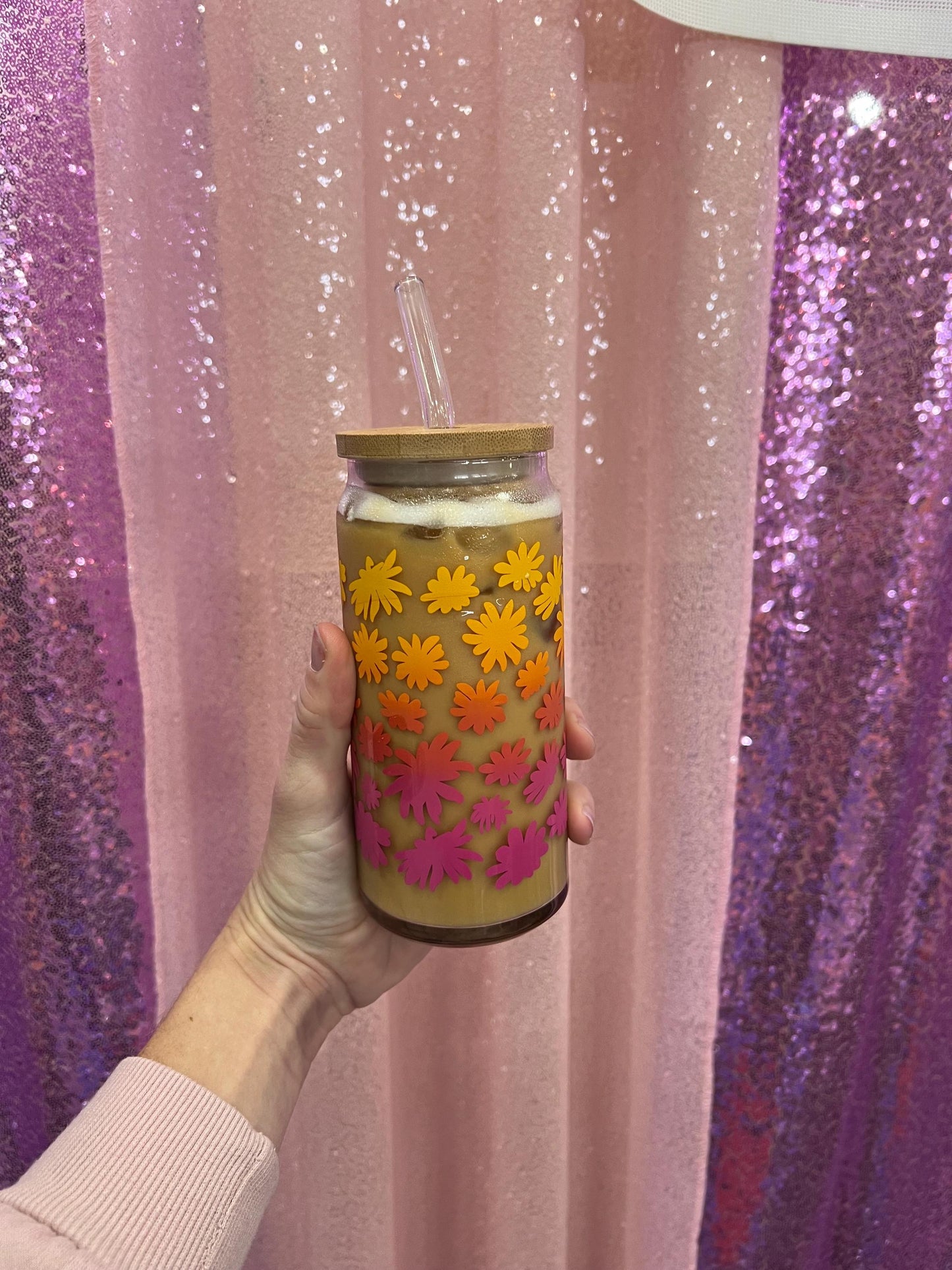 Tumbler with floral design held against a glittery pink and purple background