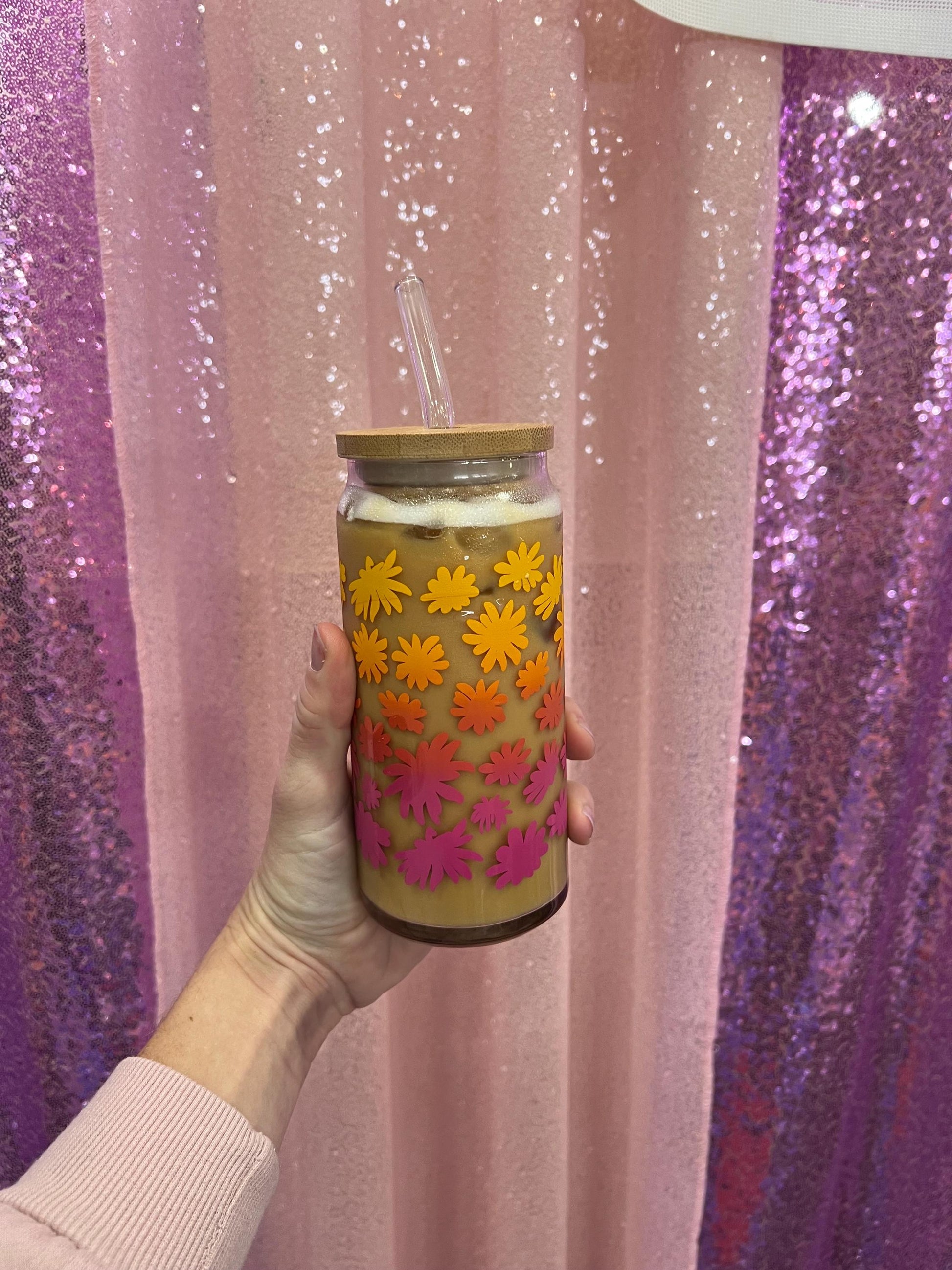 Tumbler with floral design held against a glittery pink and purple background
