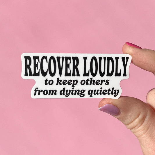 Sticker with text 'RECOVER LOUDLY to keep others from dying quietly' held by a hand against a pink background