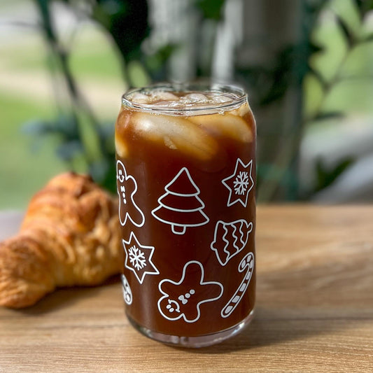Glass of iced coffee with festive designs on a wooden table outdoors.