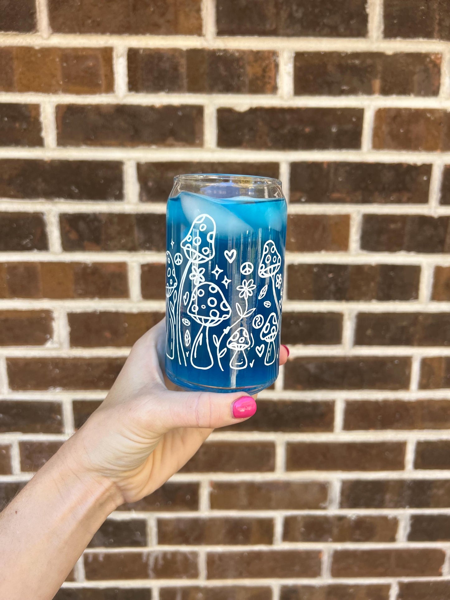 Clear glass cup with white designs held in front of a brick wall