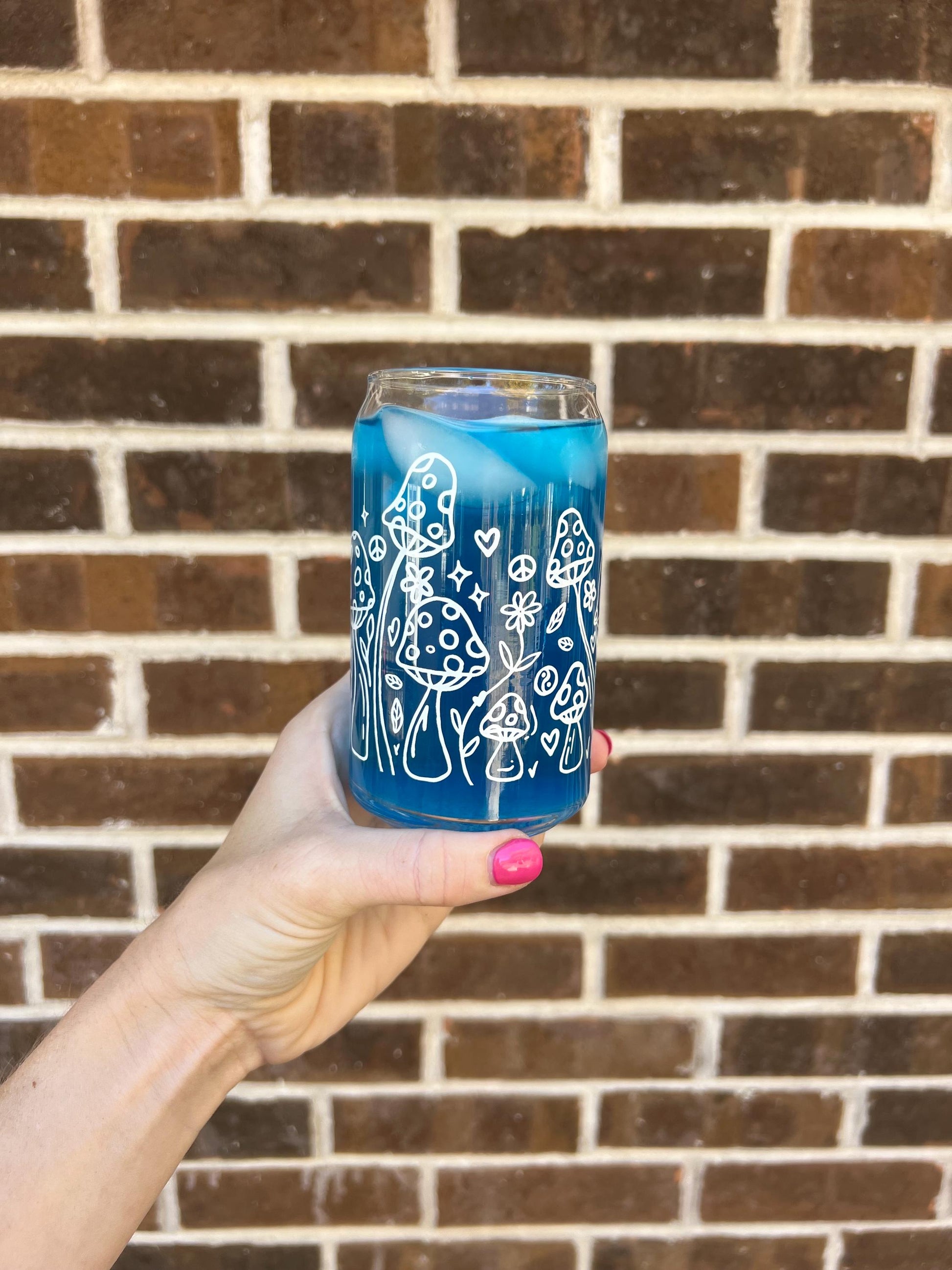 Clear glass cup with white designs held in front of a brick wall