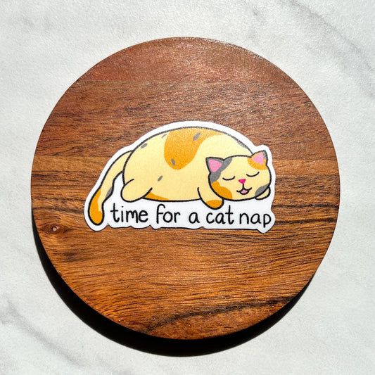 Sticker of a cat with 'time for a cat nap' text on a wooden circle