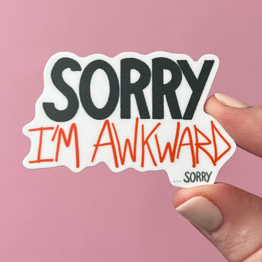 Sticker with 'Sorry I'm Awkward' text held by a hand against a pink background