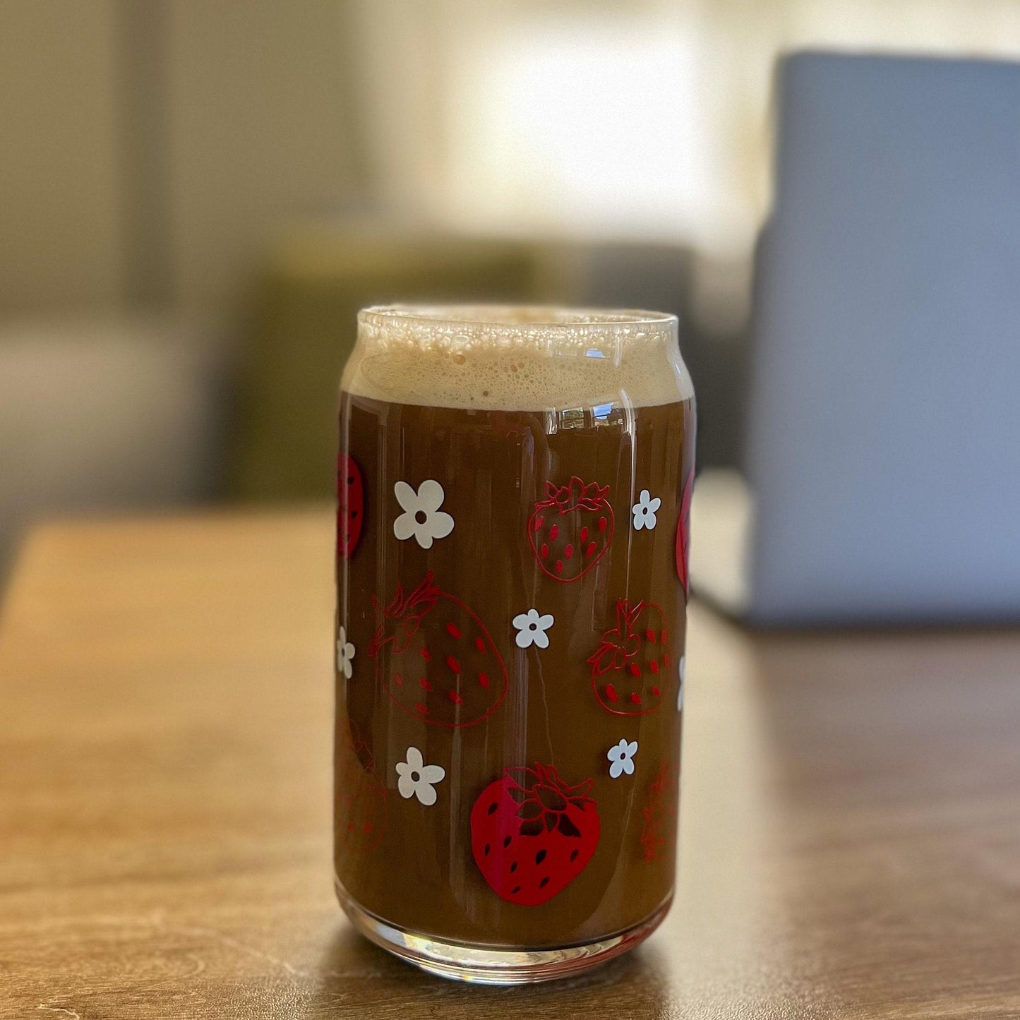 Glass of iced coffee with strawberry and white daisy design on a wooden table