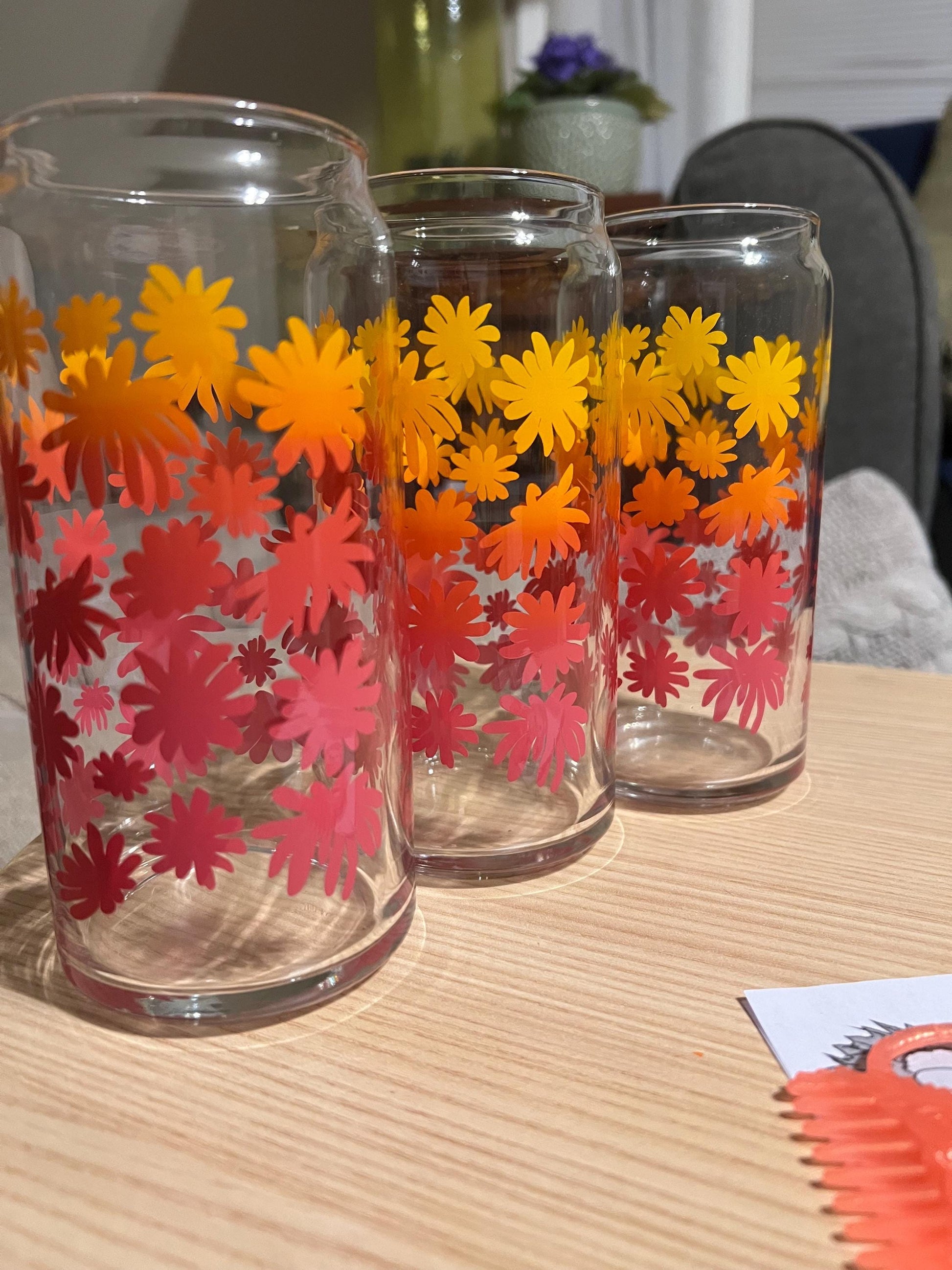 Three glass tumblers with floral designs on a wooden surface.