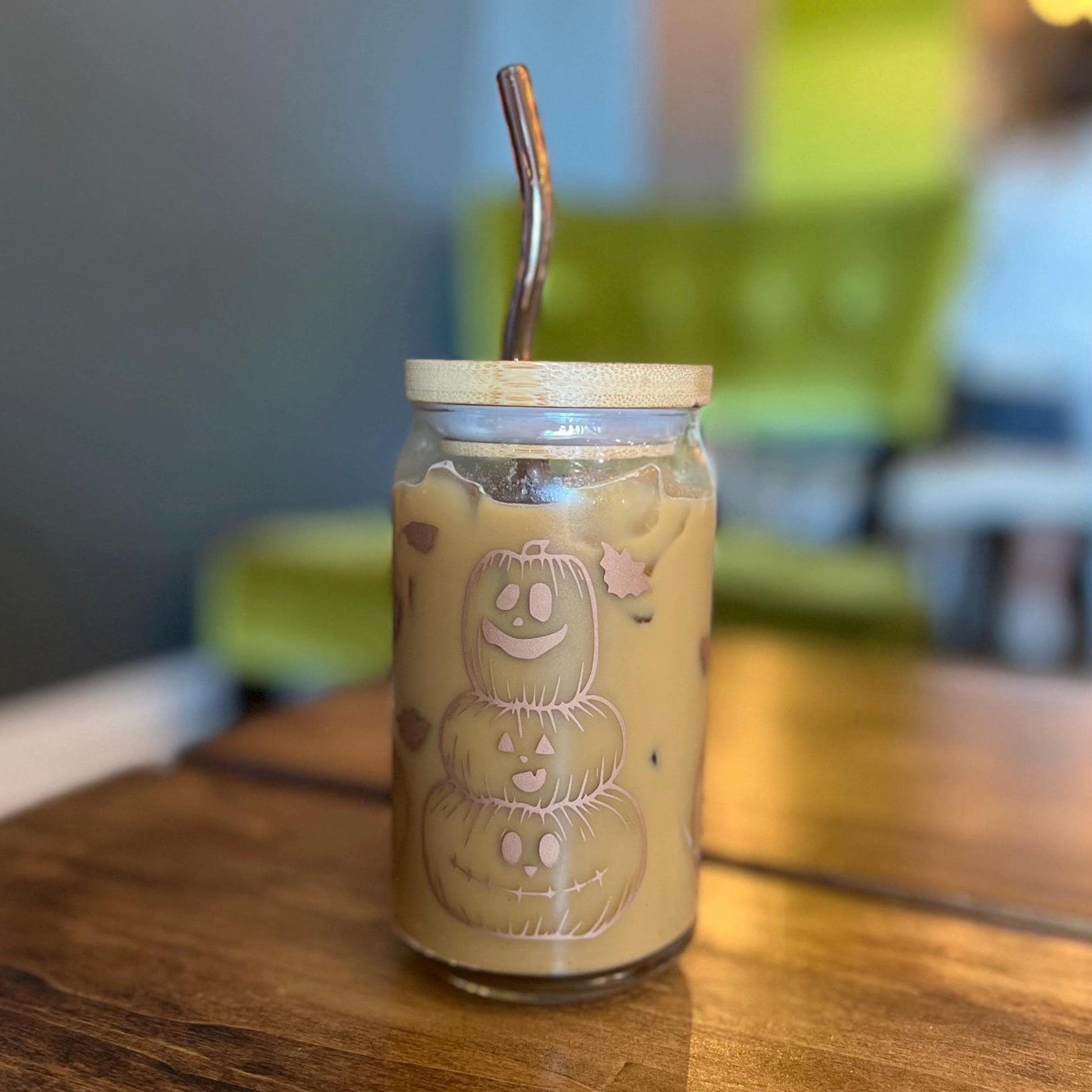 Glass jar with a lid and straw on a wooden surface, featuring a jack-o-lanterns and Halloween-themed design.