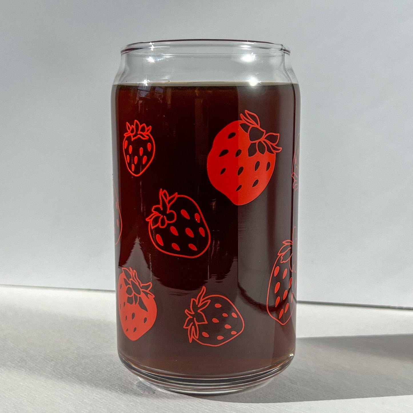 Clear glass can with red strawberry illustrations on a white background