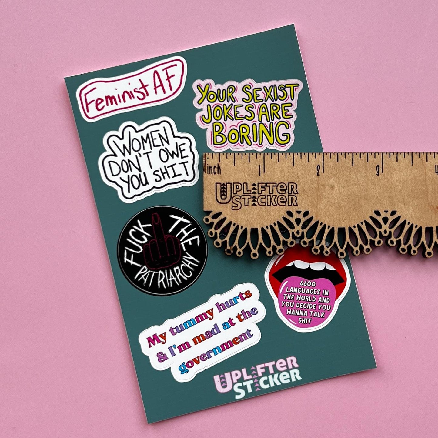 Sticker pack with various statements on a pink background, next to a ruler for size reference.