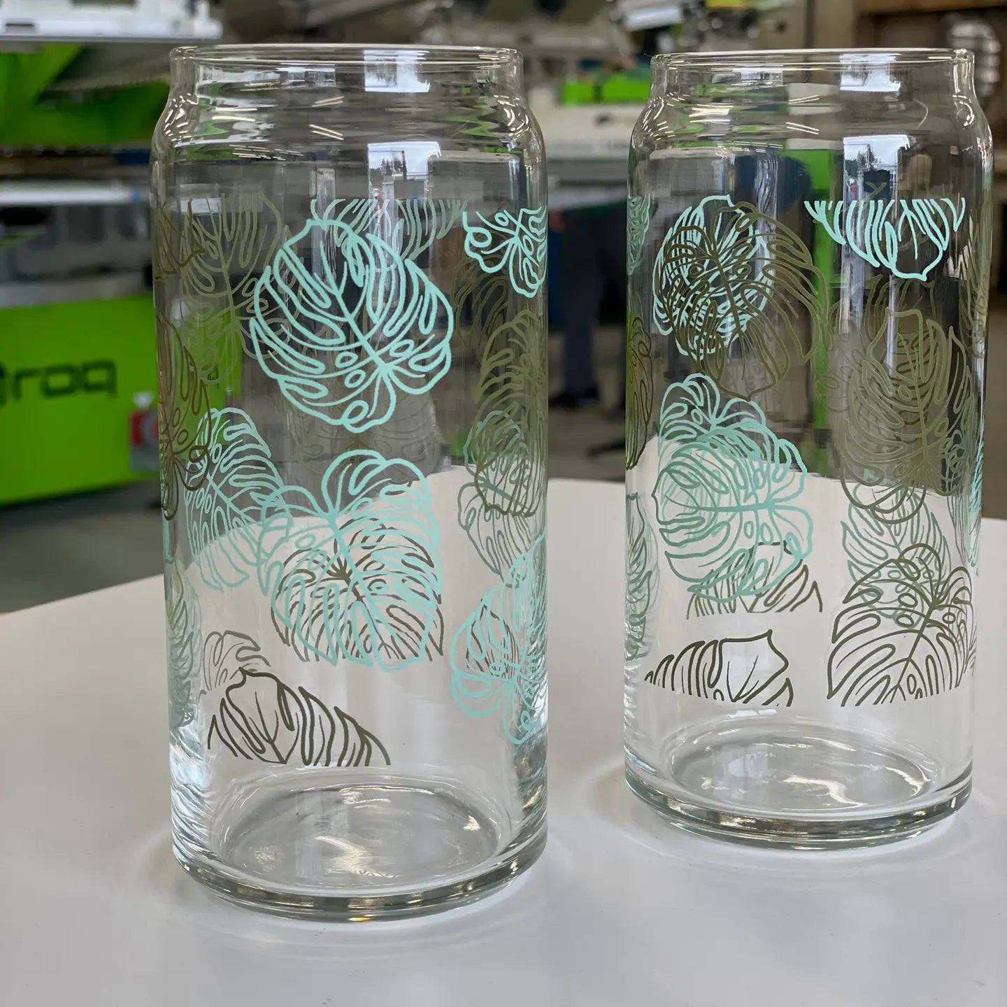 Two glass tumblers with monstera patterns on a white surface.