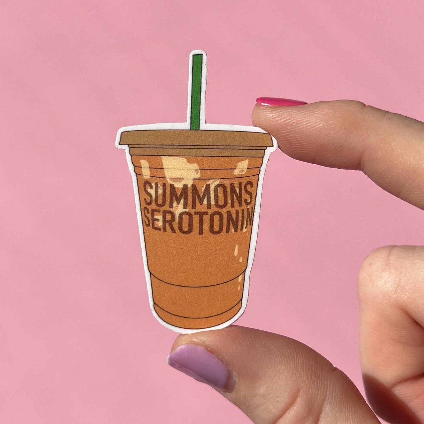 Sticker of a coffee cup with 'Summons Serotonin' text held by a hand against a pink background