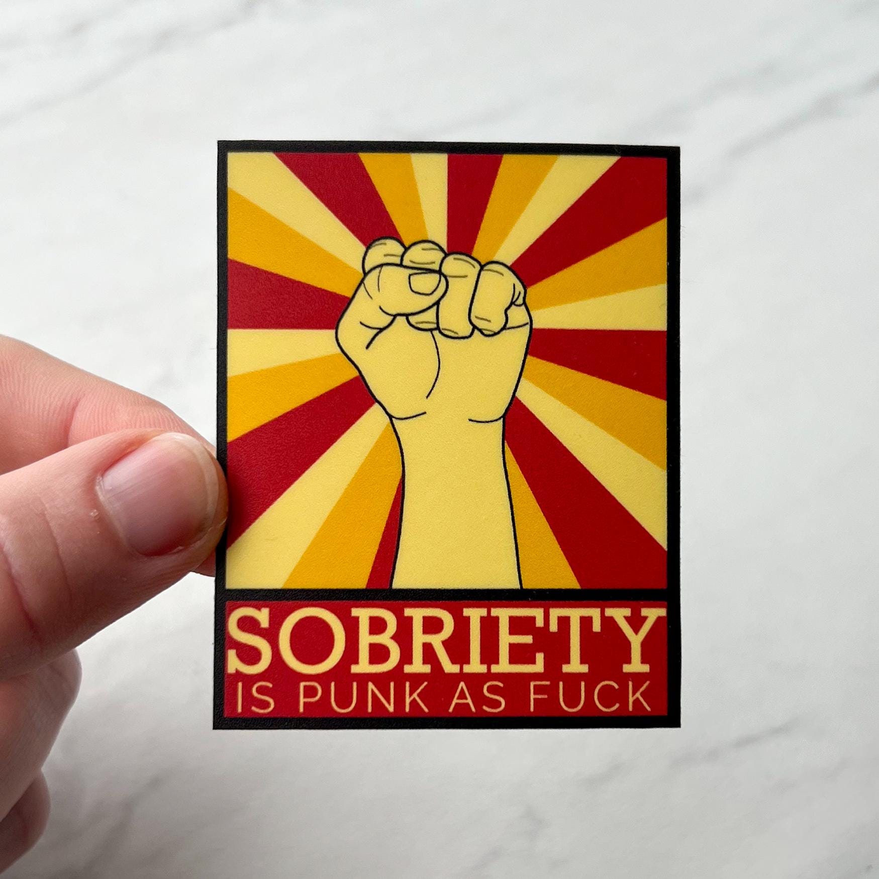 Sticker with a fist graphic and text 'Sobriety is punk as fuck' held by a hand on a white background