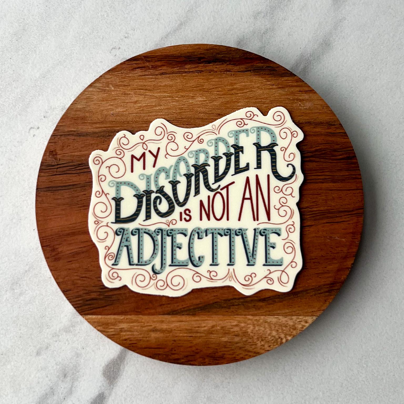 Wooden coaster with decorative sticker that reads ''my disorder is not an adjective' on a marble surface