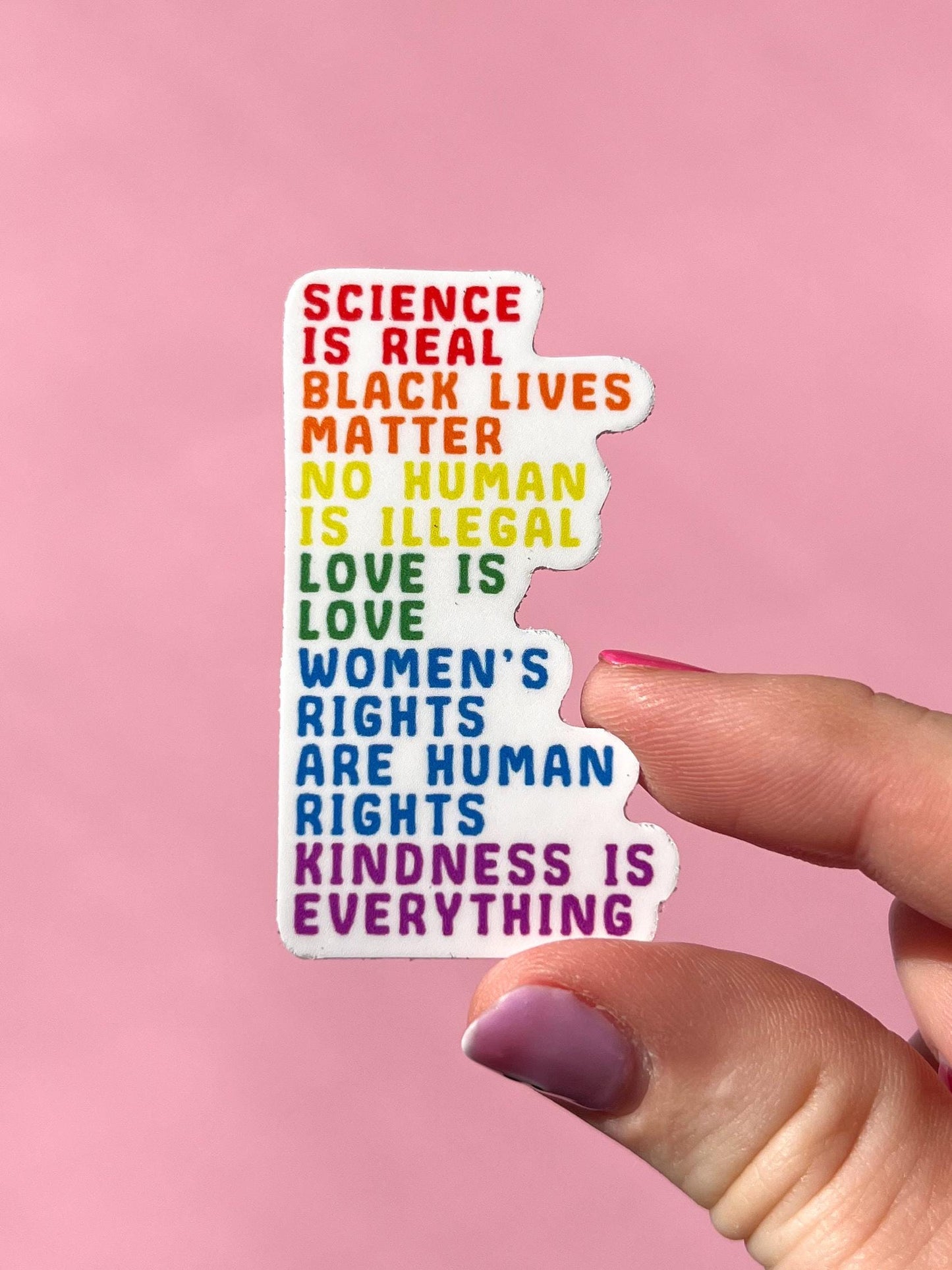 Hand holding a colorful sticker with social justice messages on a pink background