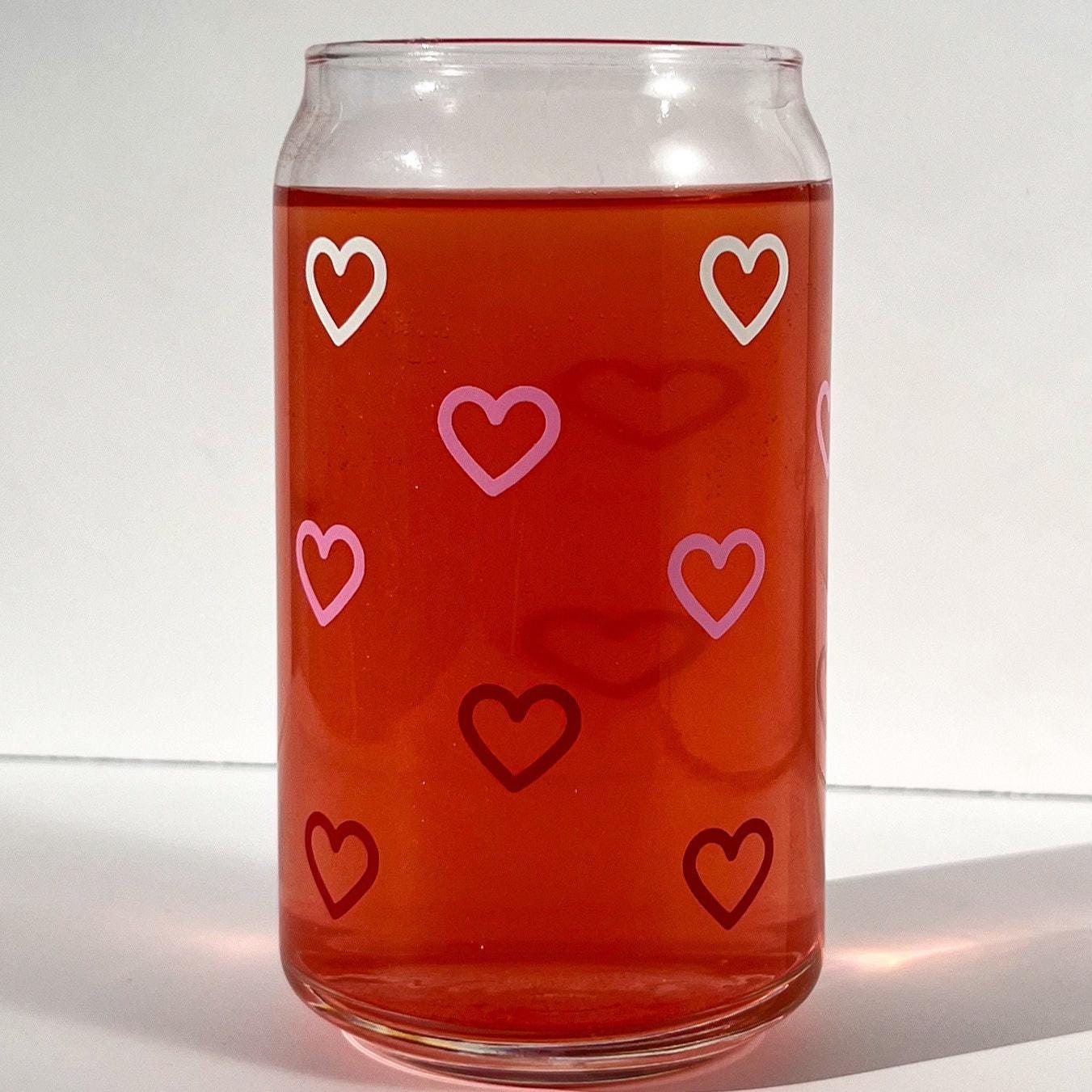 Clear glass can with white, pink and red heart patterns filled with a red liquid on a white background