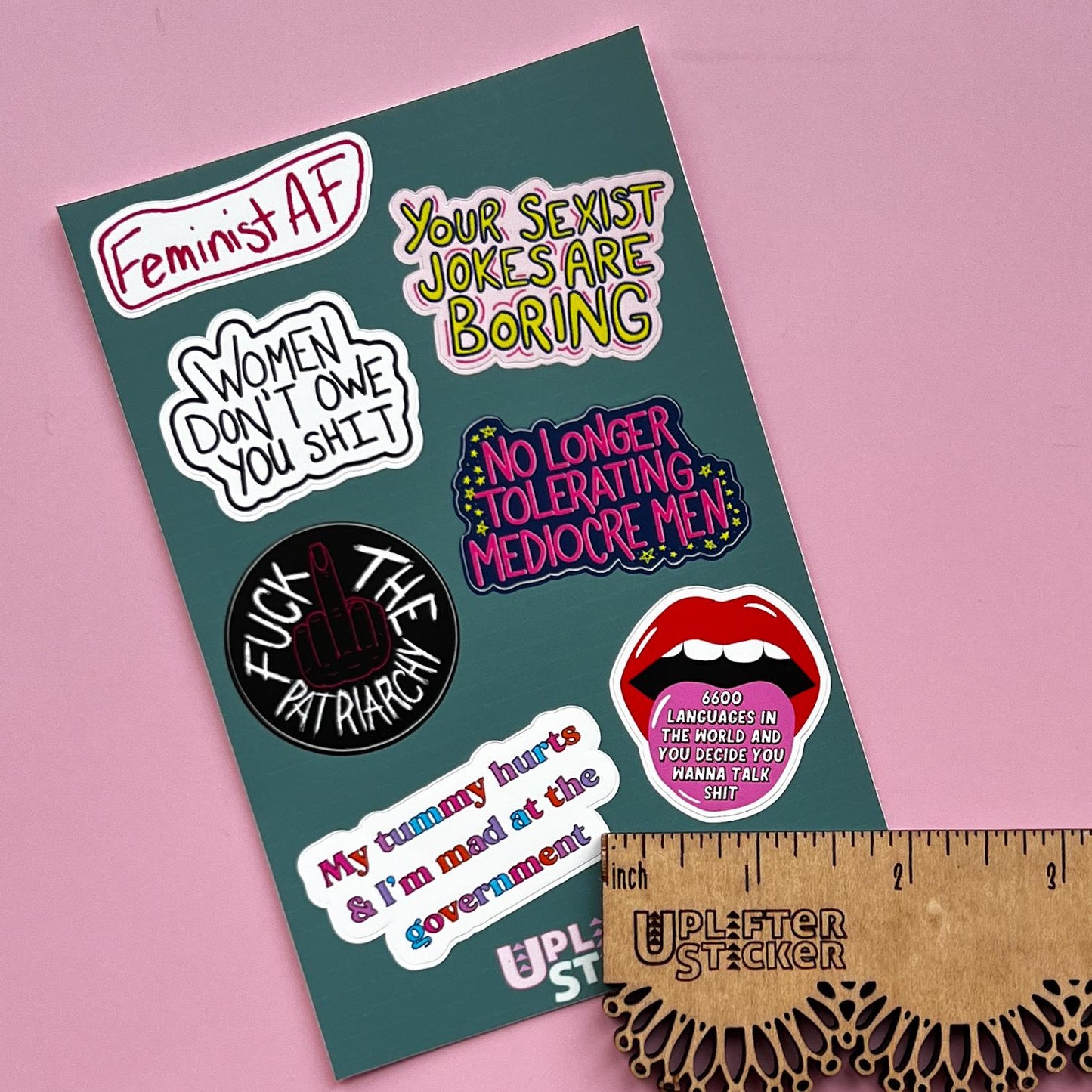 Sticker pack with various statements on a pink background, next to a ruler for size reference.