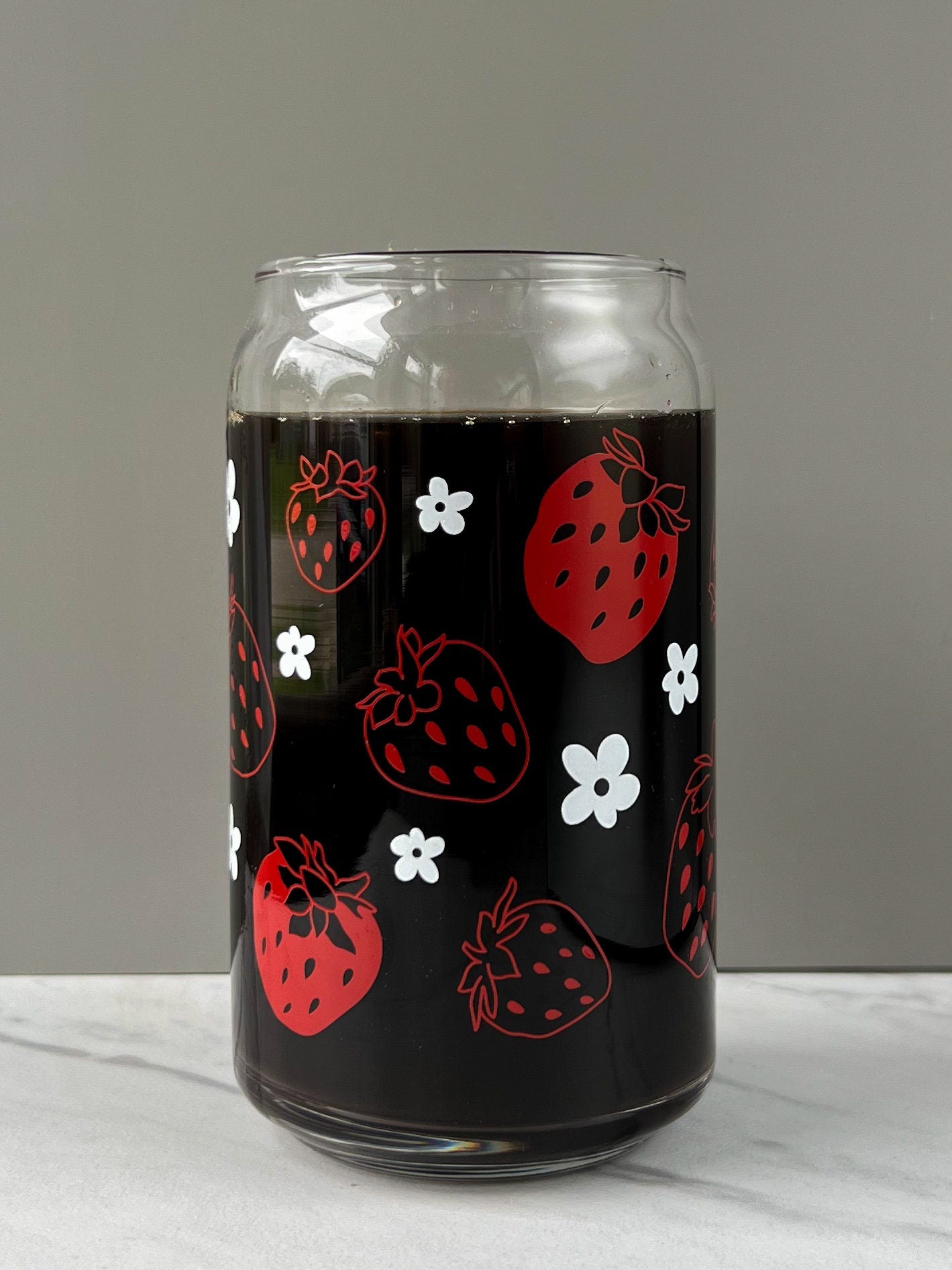 Glass jar with coffee and red strawberry and white daisy pattern on a gray background