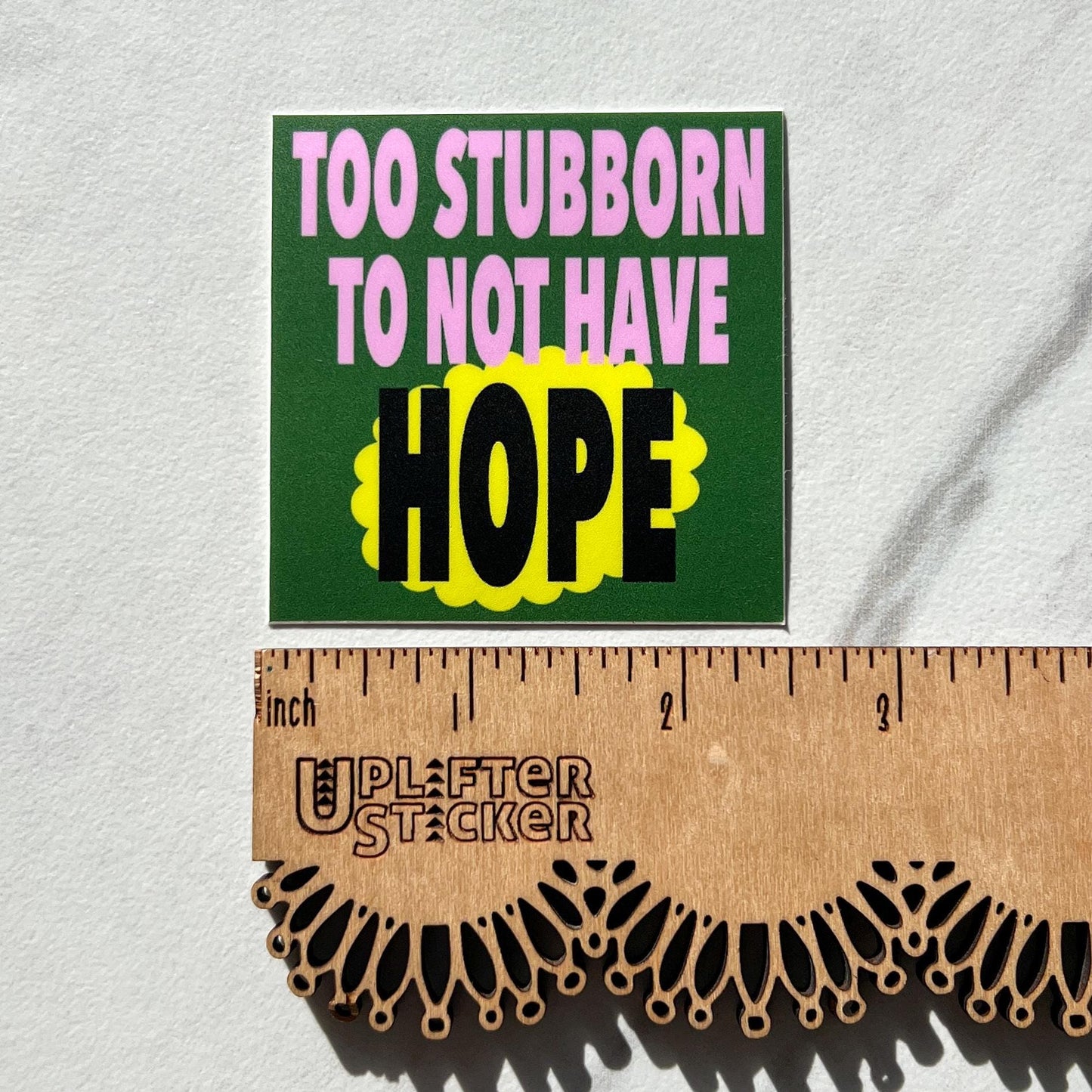 Sticker with 'Too Stubborn to Not Have Hope' text on a white background with a ruler for scale.