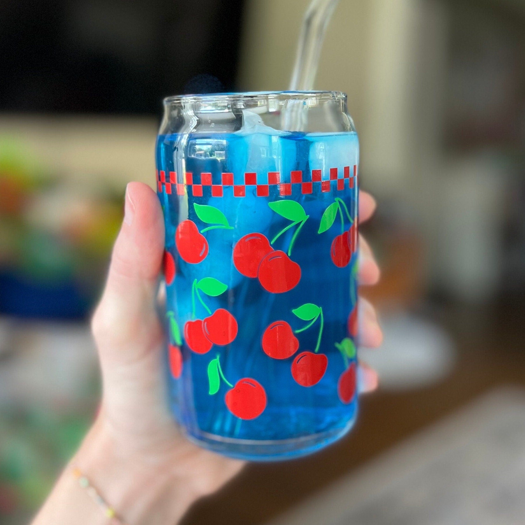 Hand holding a clear glass with cherry design filled with a blue liquid.