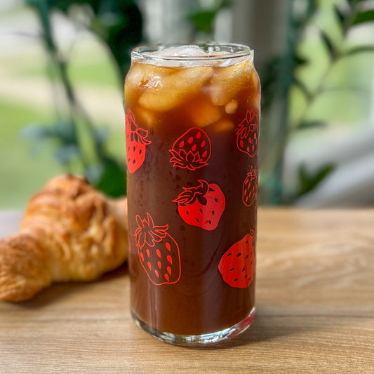 Glass of iced coffee with strawberry design on a wooden table with a croissant.