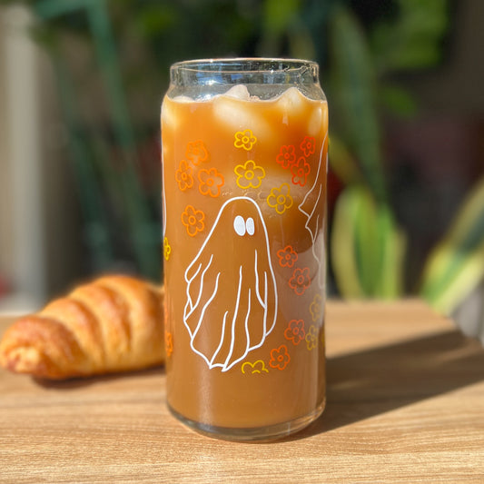 Glass of iced coffee with a ghost and vintage flower design on a wooden table with a croissant.