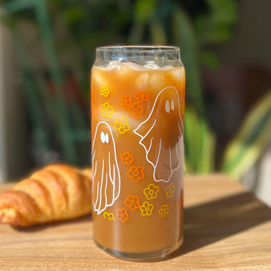 Glass of iced coffee with ghost and flower designs on a wooden table with a croissant.