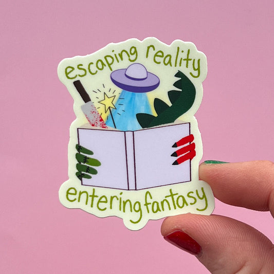 Sticker with 'escaping reality entering fantasy' text held by a hand on a pink background