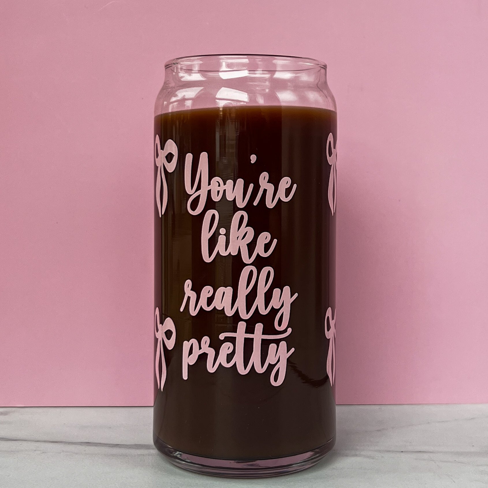 Glass can with pink text that reads "you're like really pretty" with pink bows on a pink background