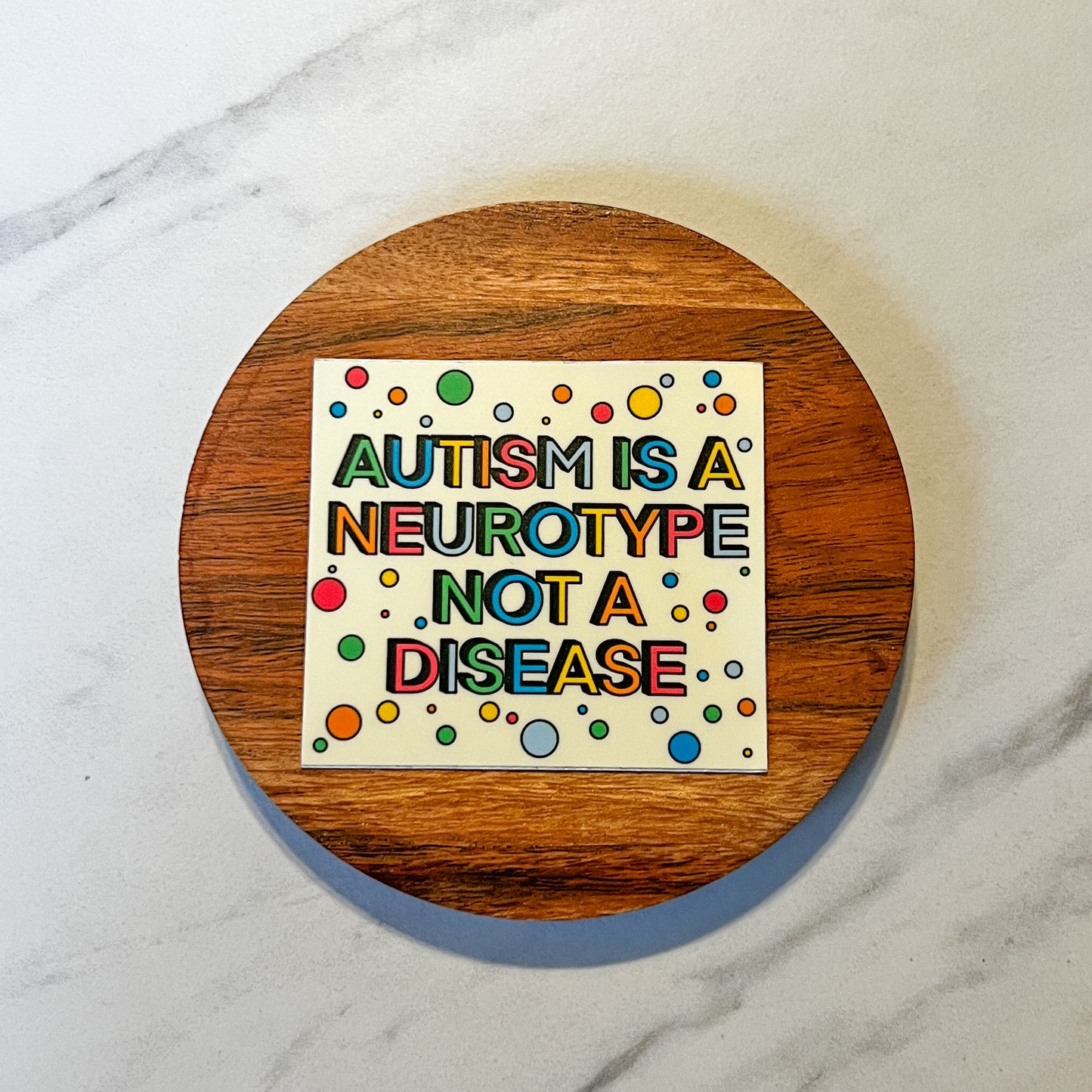 Colorful sign on a wooden round object with text 'Autism is a neurotype not a disease' on a marble background