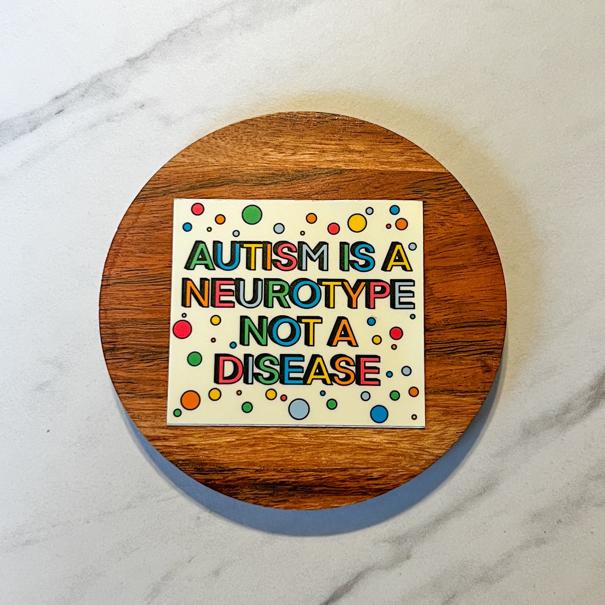 Colorful sign on a wooden round object with text 'Autism is a neurotype not a disease' on a marble background