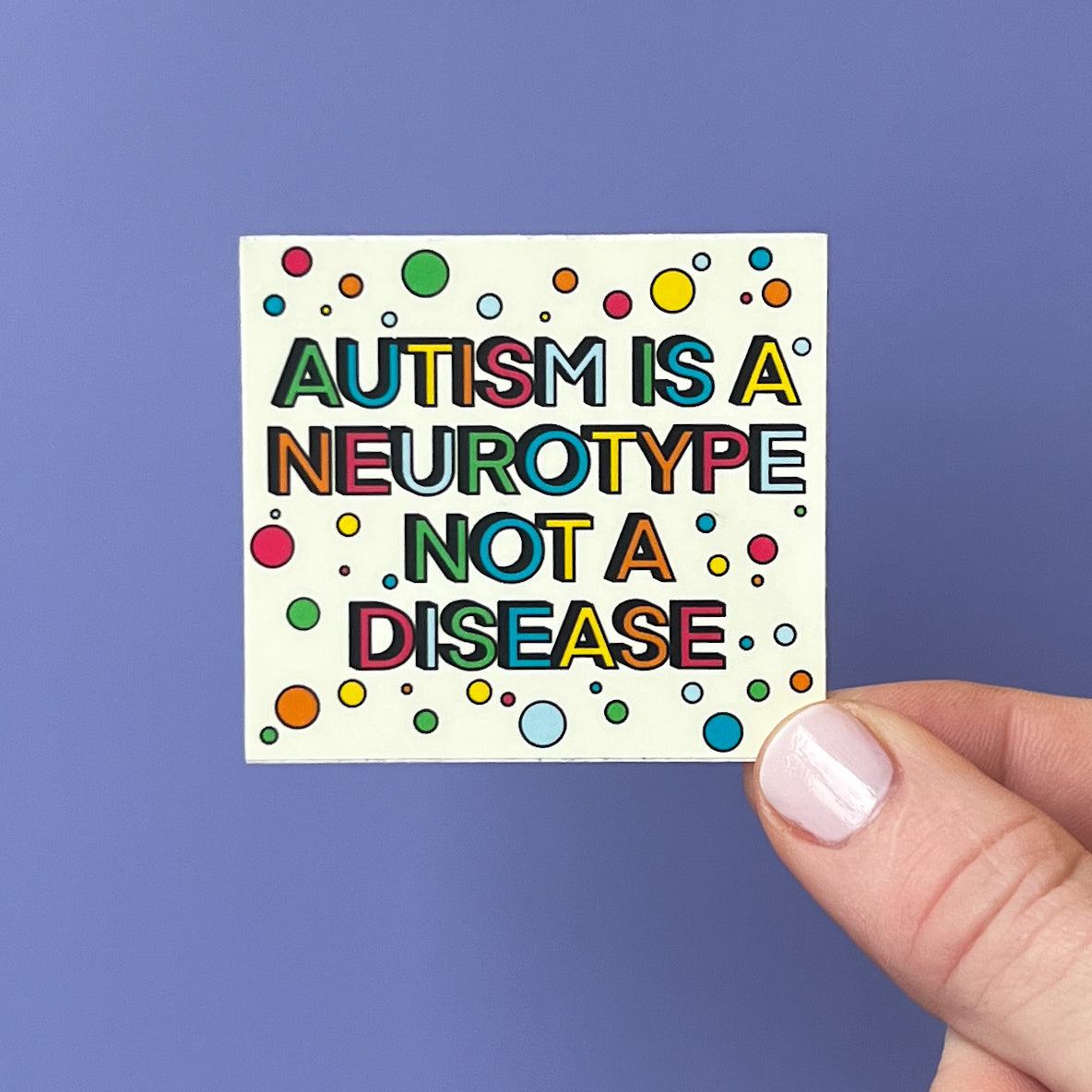 Hand holding a colorful sticker with text 'Autism is a neurotype not a disease' against a blue background