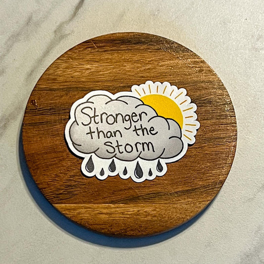 Round wooden coaster with a motivational sticker featuring a cloud and sun design on a beige background.