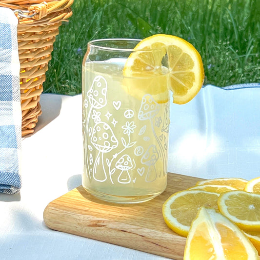 Glass with doodled mushrooms on it lemon slices on a wooden board outdoors