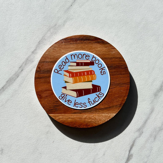 Round wooden coaster with a sticker featuring books and text that reads 'read more books' on a light gray background
